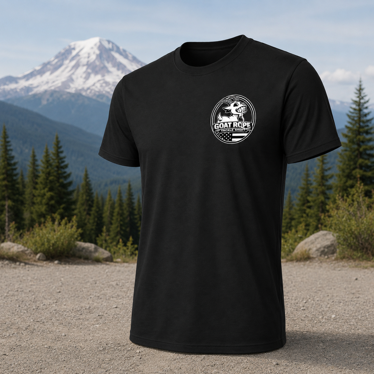 A black short-sleeve crewneck t-shirt with a white circular 'GOAT RIDE' logo printed on the left chest, displayed against a scenic outdoor background of a snowy mountain, pine trees, and a gravel path.