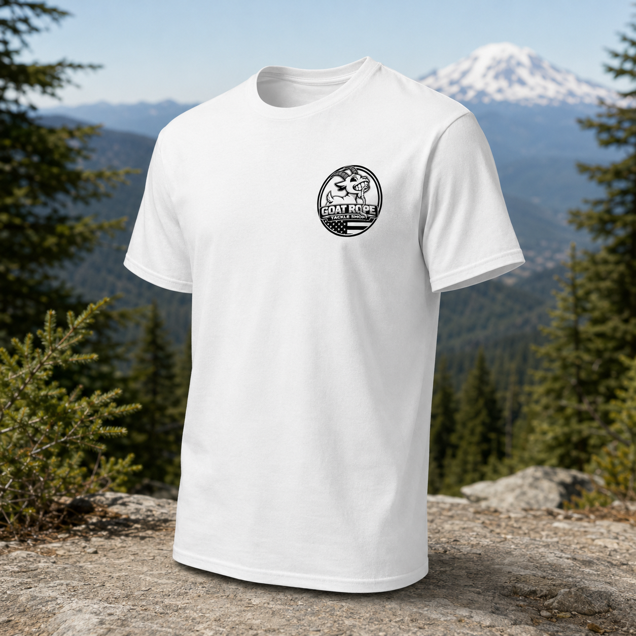 A white short-sleeve crewneck t-shirt with a black circular 'Goat Rest' logo on the left chest, displayed on a rocky mountain peak with pine trees and a snow-capped mountain in the background.