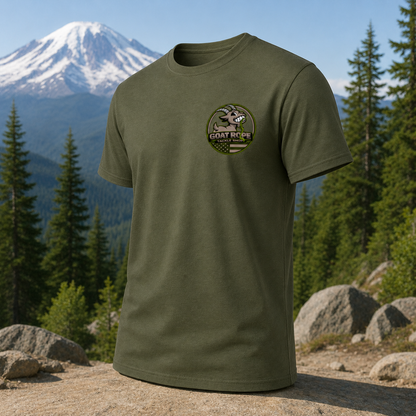 An olive green short-sleeve t-shirt with a circular 'Goat Rope' logo on the left chest, displayed against a scenic background of a snow-capped mountain, pine trees, and rocks.