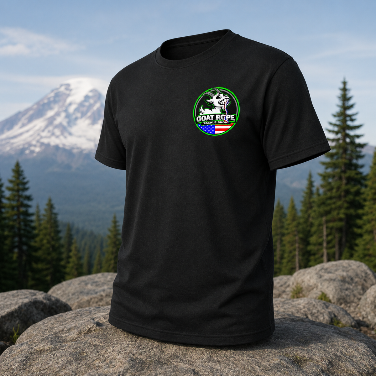 A black short-sleeve t-shirt with a circular 'GOAT REPE' graphic on the left chest, displayed on a large rock with a mountain and pine forest background.