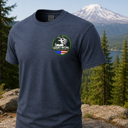 A heather navy blue short-sleeve t-shirt with a circular green, white, and red 'GOAT ROPE' logo on the left chest, displayed against a blurred mountain and forest background.