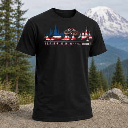 A black short-sleeve graphic t-shirt displayed against a scenic mountain and forest background. A black short-sleeve crewneck t-shirt featuring a graphic print of a mountain and fishing tackle shop in a stylized American flag pattern, with the text 'GOAT ROPE TACKLE SHOP - PORT Orchard WA' printed below.