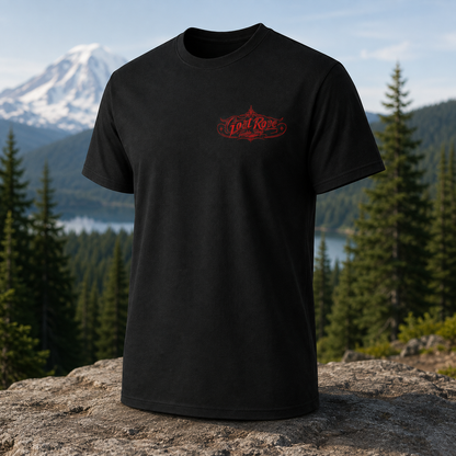 A black short-sleeve t-shirt with a red 'Goat Rope' graphic on the left chest, displayed on a rock with a mountain and forest background.